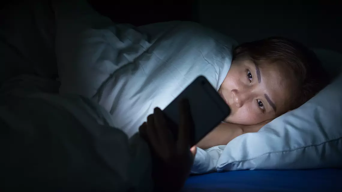 une adolescente qui consulte son smartphone dans son lit à des heures tardives